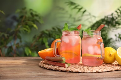 Photo of Mason jars of tasty rhubarb cocktail with citrus fruits on wooden table outdoors, space for text