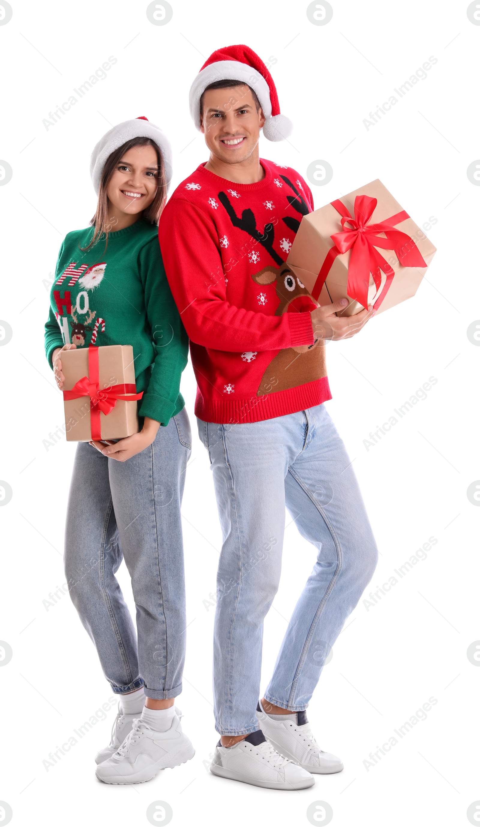 Photo of Beautiful happy couple in Santa hats and sweaters holding Christmas gifts on white background