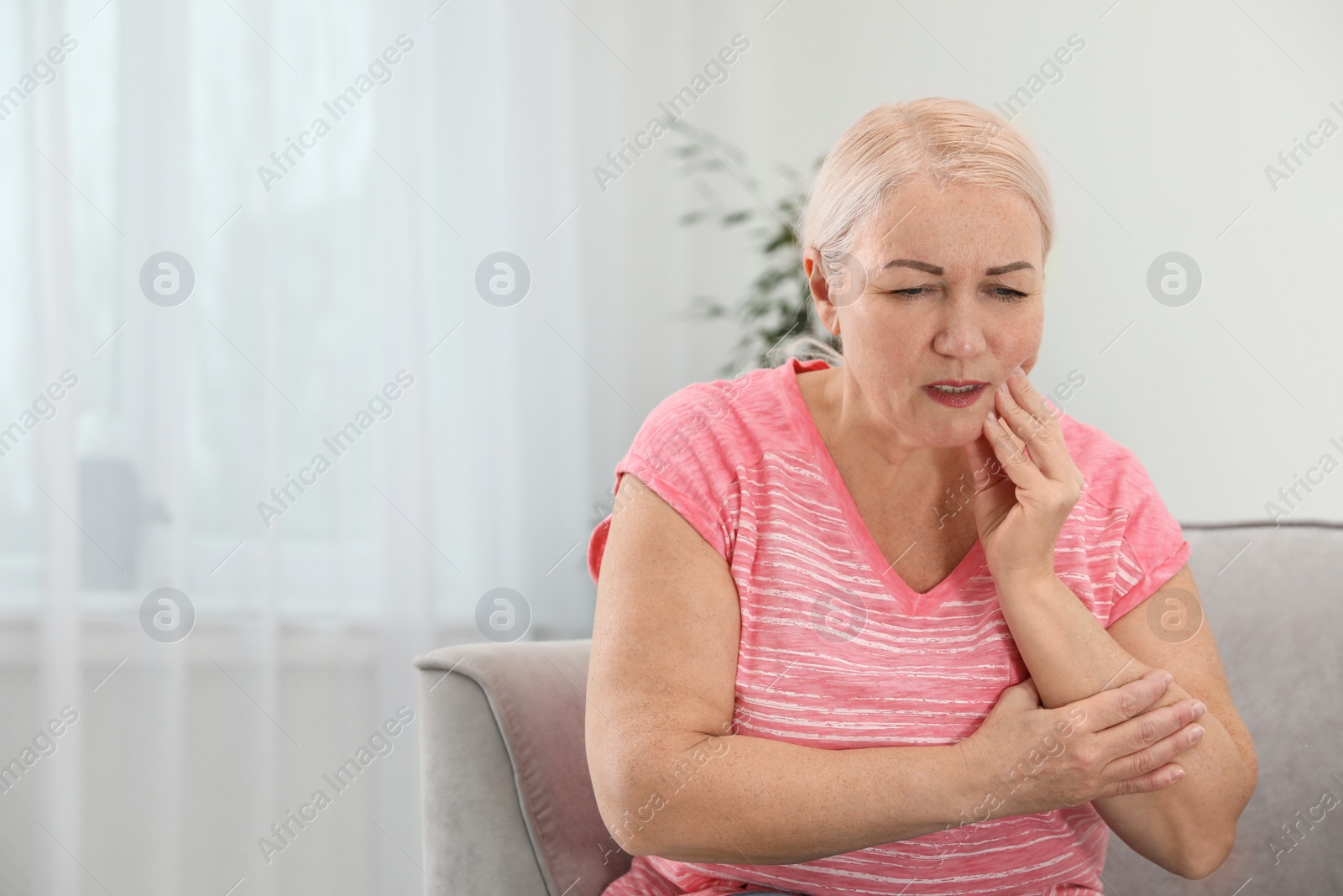 Photo of Mature woman suffering from strong tooth pain at home, space for text