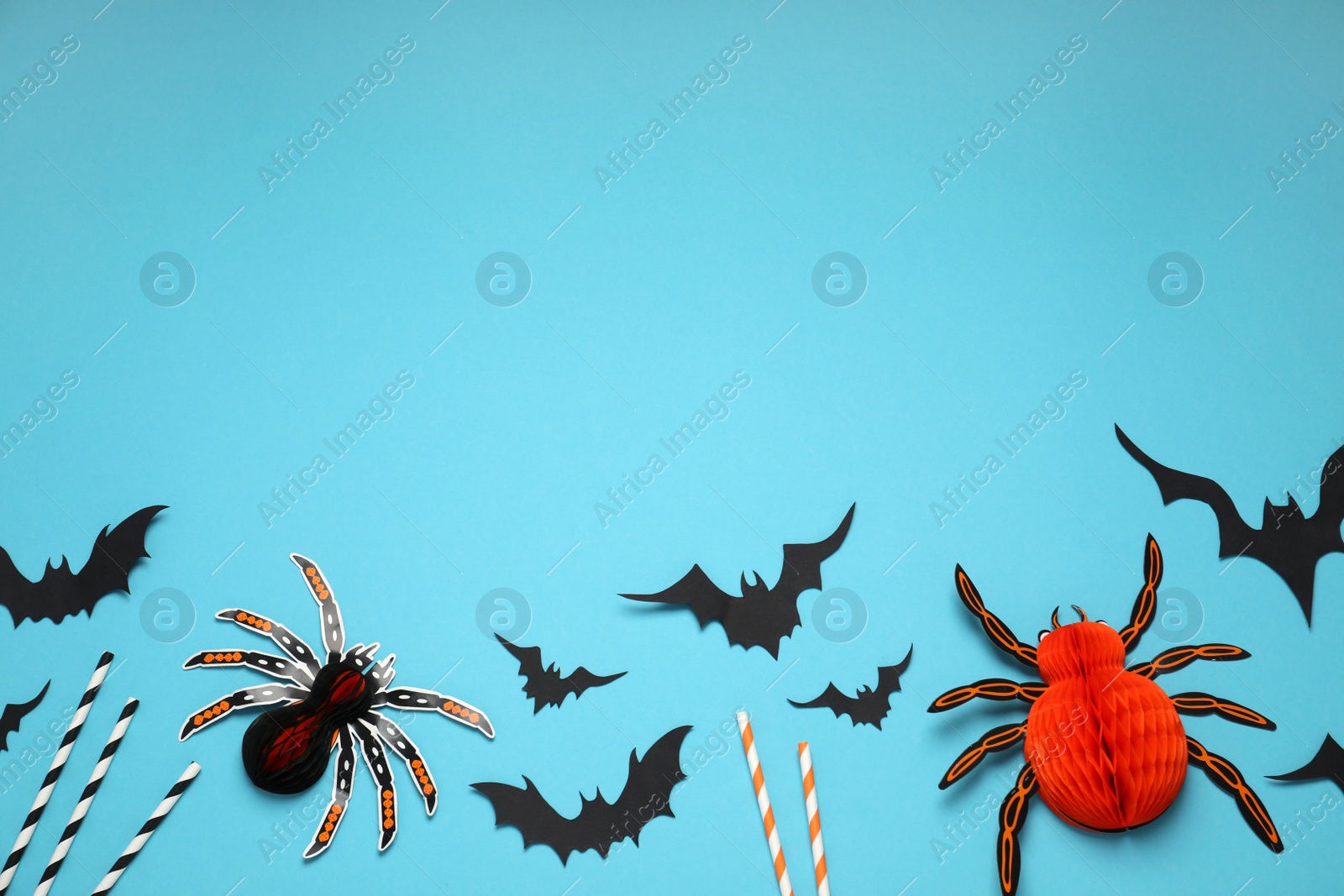 Photo of Flat lay composition with paper bats, spiders and cocktail straws on light blue background, space for text. Halloween decor