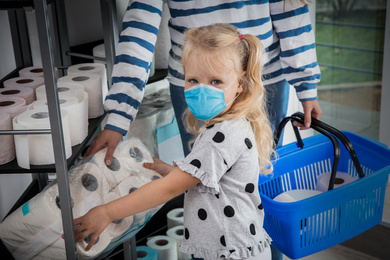 Image of Little girl with medical mask and mother buying toilet paper in shop
