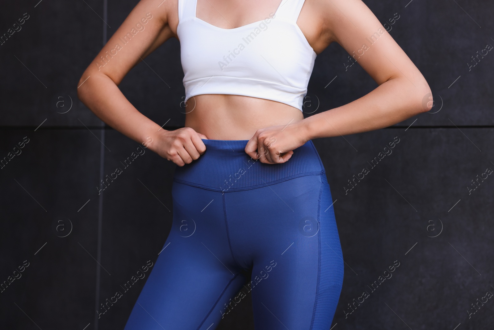 Photo of Woman in sportswear near dark grey wall, closeup