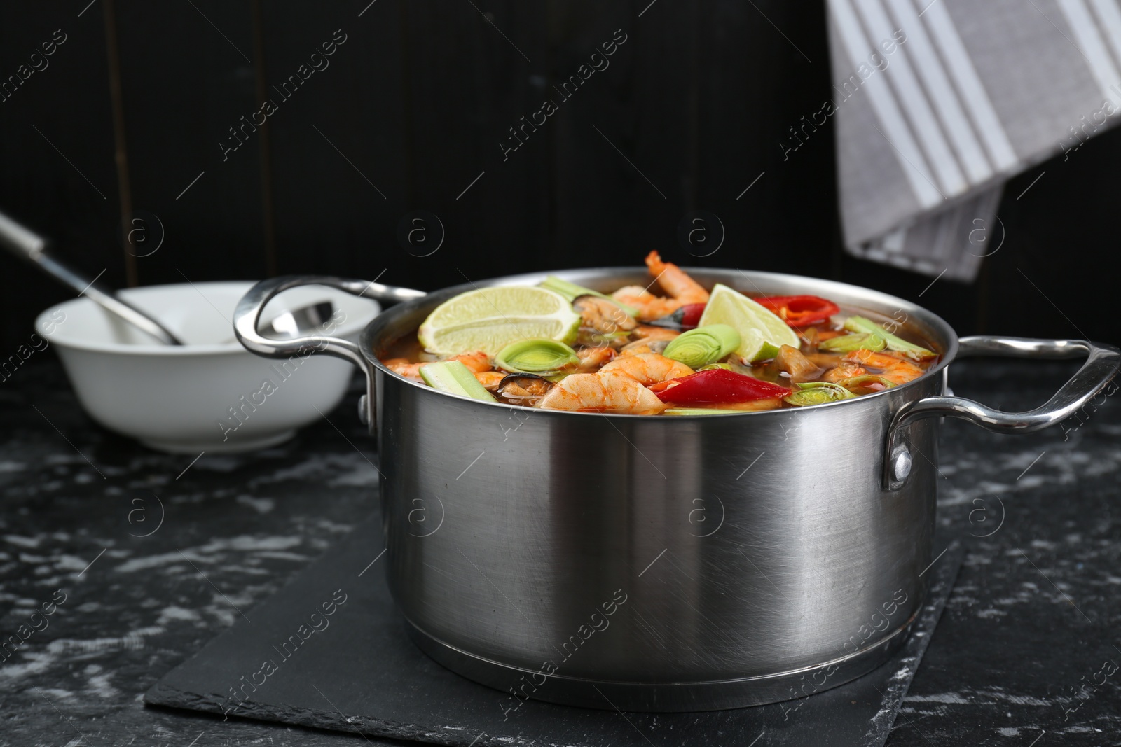 Photo of Saucepan with delicious Tom Yum soup on black marble table