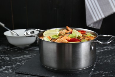 Saucepan with delicious Tom Yum soup on black marble table