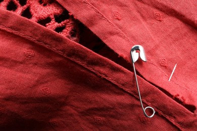 Photo of Metal safety pin on red fabric, closeup