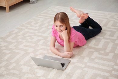 Photo of Teenage girl with laptop lying on cozy carpet at home