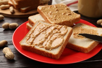 Photo of Delicious toasts with peanut butter, nuts and knife on dark wooden table, closeup