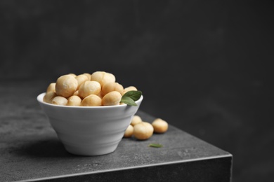 Bowl with shelled organic Macadamia nuts on table against dark background. Space for text