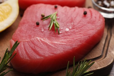 Photo of Raw tuna fillet with rosemary and peppercorns on board, closeup