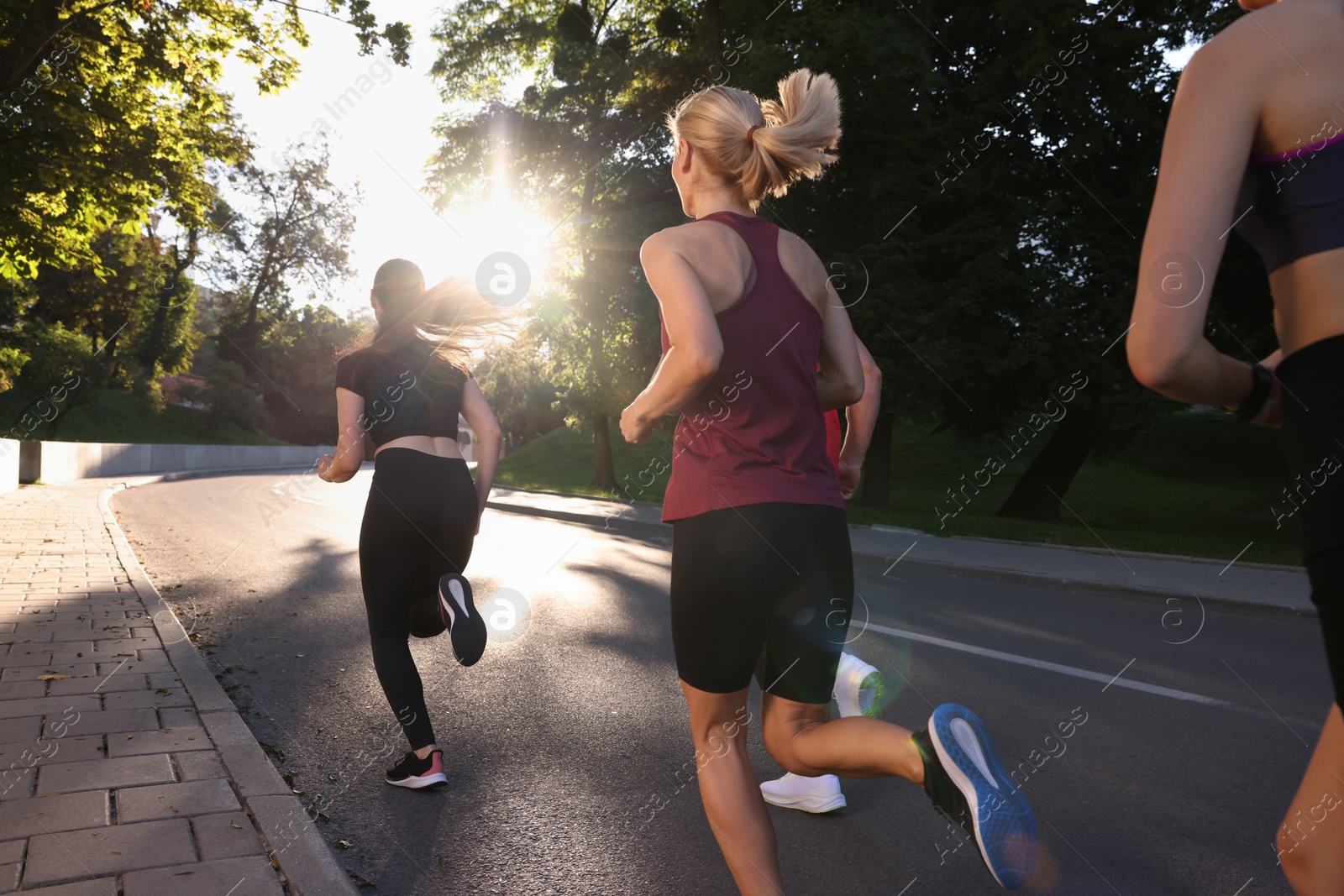 Photo of Group of people running outdoors on sunny day, back view