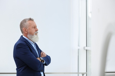 Photo of Portrait of handsome mature man in elegant suit looking out window indoors