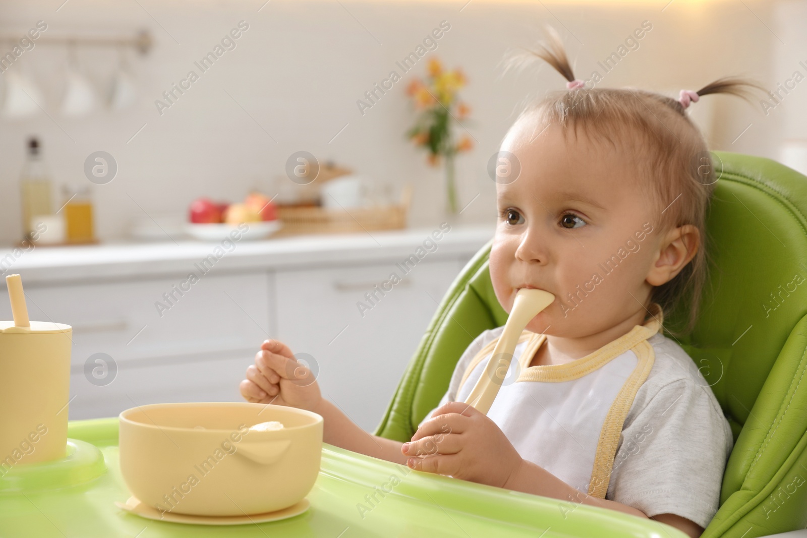 Photo of Cute little baby eating food in high chair at kitchen