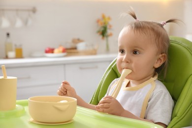 Cute little baby eating food in high chair at kitchen