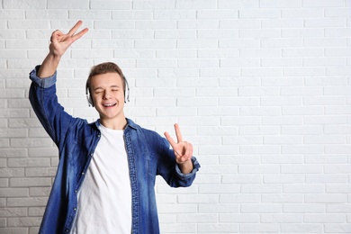 Teen boy listening to music with headphones near brick wall, space for text