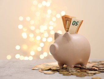 Photo of Piggy bank with euro banknote and coins on grey table against blurred lights