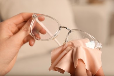 Photo of Woman cleaning glasses with microfiber cloth at home, closeup