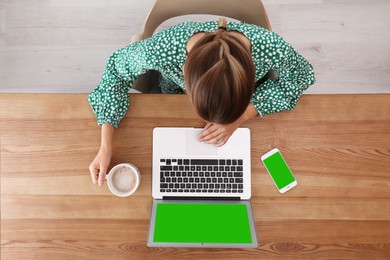 Woman using with laptop at wooden table, top view. Devices displays with chroma key