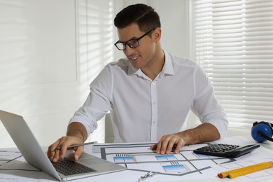 Photo of Architect working with construction drawings and laptop in office
