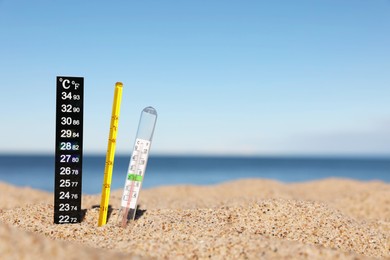 Weather thermometers in sand near sea, space for text