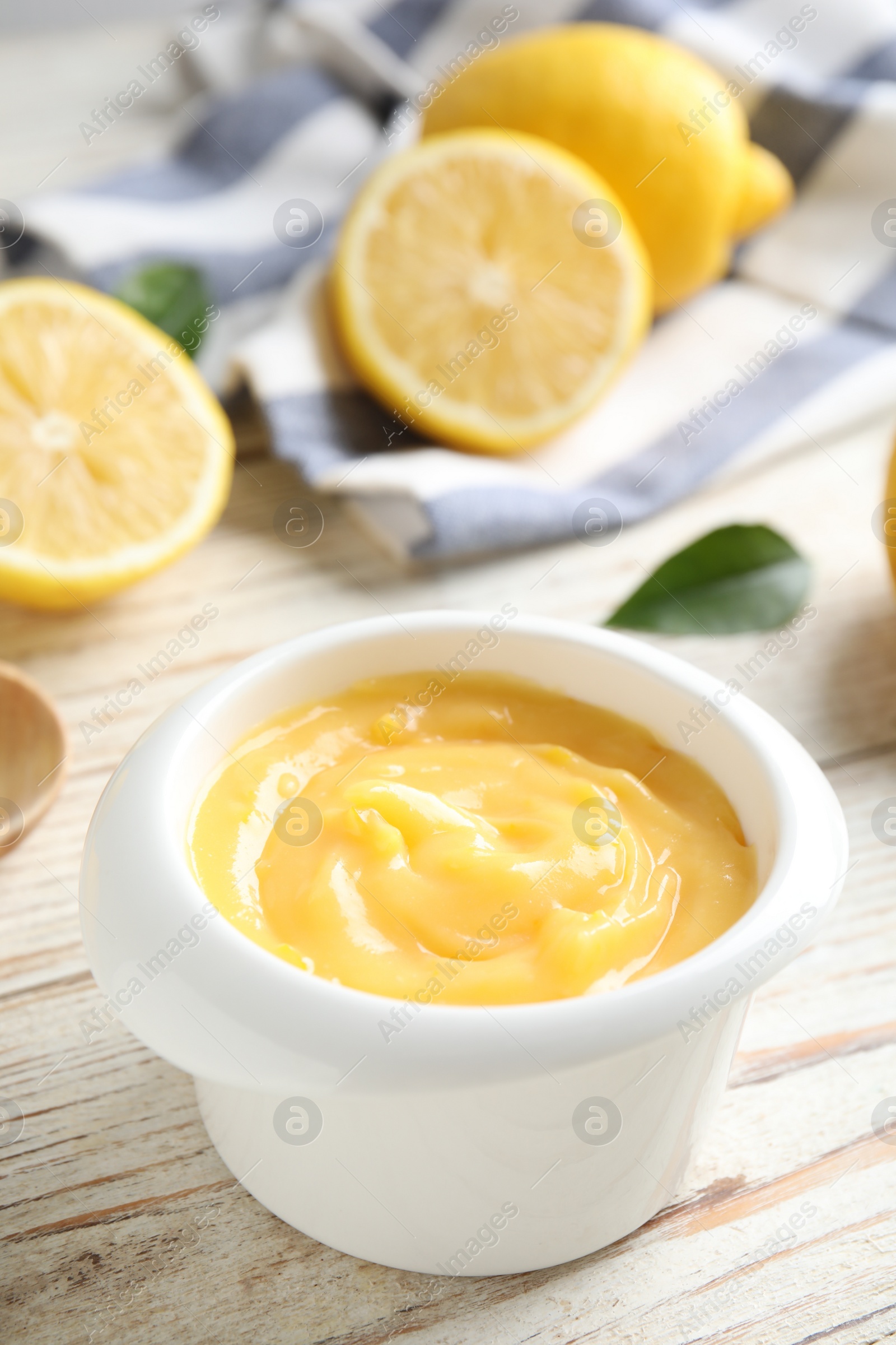 Photo of Delicious lemon curd in bowl on white wooden table, closeup