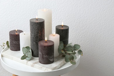 Set of burning candles and green branches on table at white wall, space for text