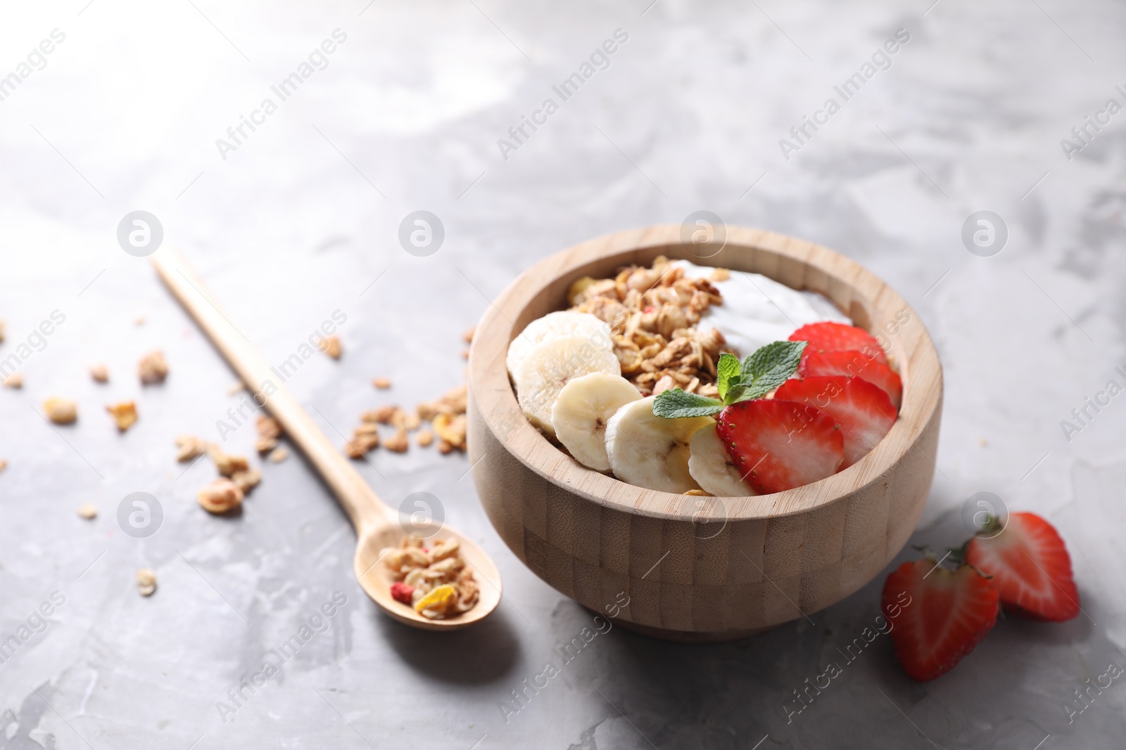 Photo of Tasty granola in bowl served on gray textured table, closeup