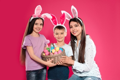 Photo of Cute family in bunny ears headbands with basket of Easter eggs on color background