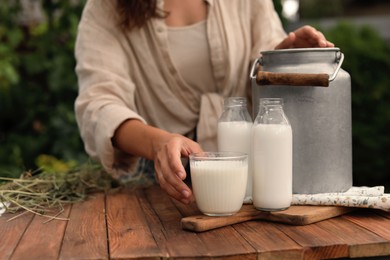 Photo of Woman taking glass with fresh milk at wooden table outdoors, closeup