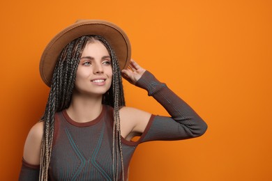 Photo of Beautiful woman with long african braids and hat on orange background, space for text