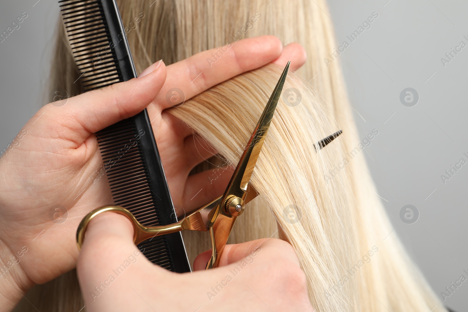 Photo of Hairdresser cutting client's hair with scissors on light grey background, closeup