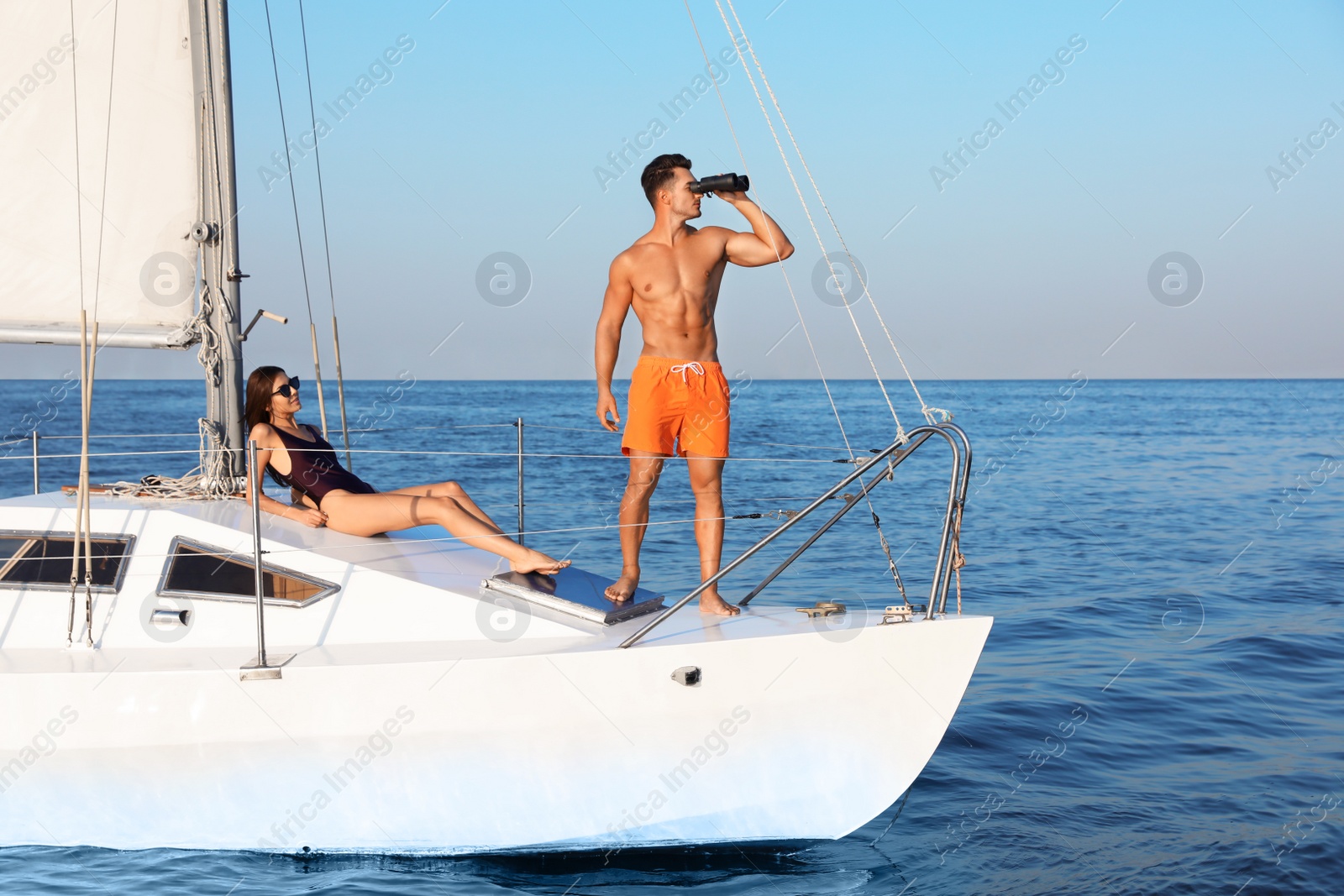 Photo of Young man and his beautiful girlfriend in bikini on yacht. Happy couple during sea trip