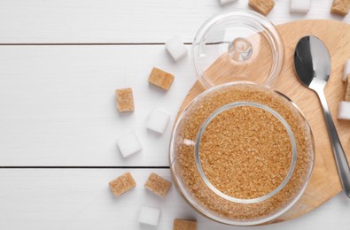 Photo of Brown sugar in jar and spoon on white wooden table, top view. Space for text