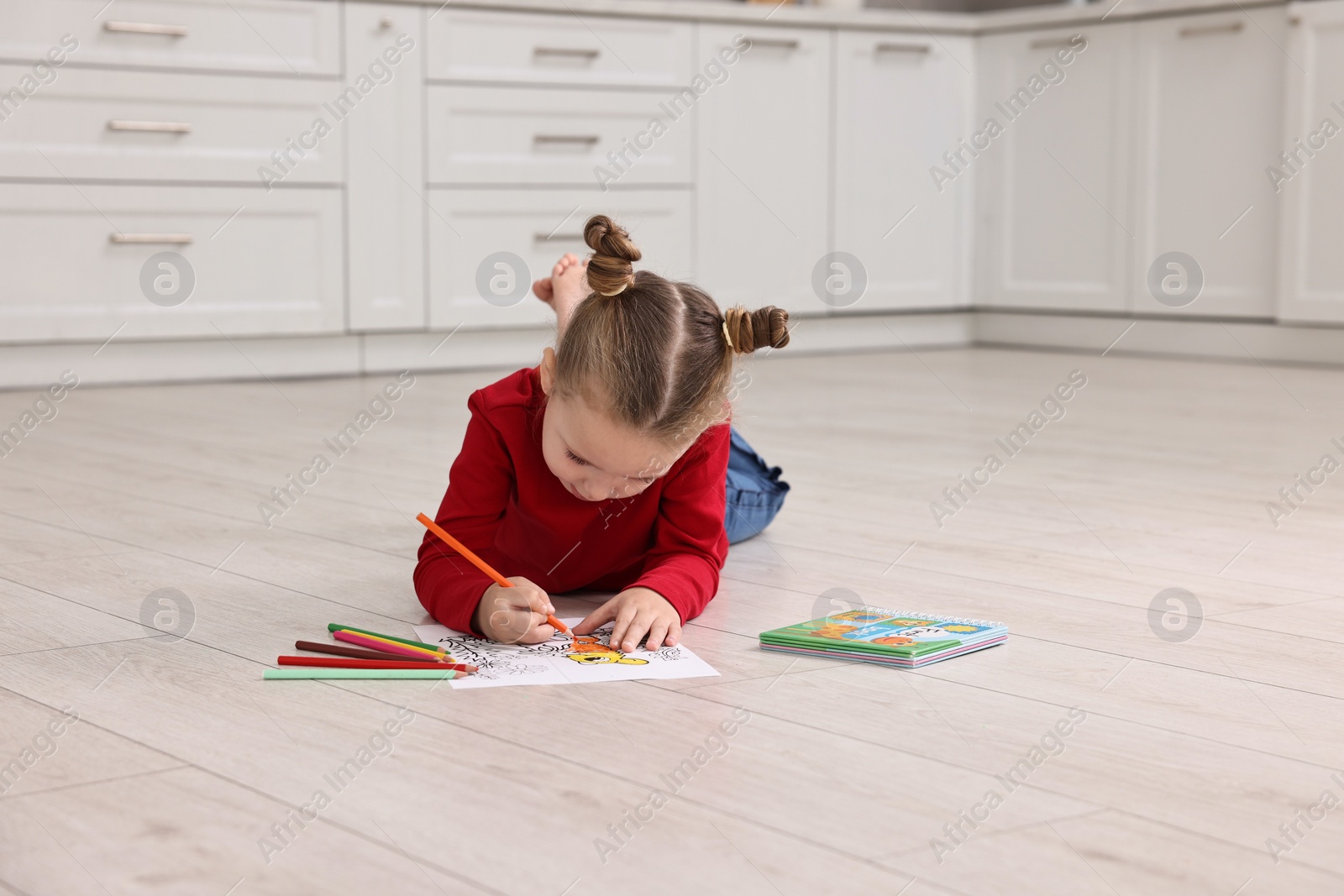 Photo of Cute little girl coloring on warm floor in kitchen. Heating system