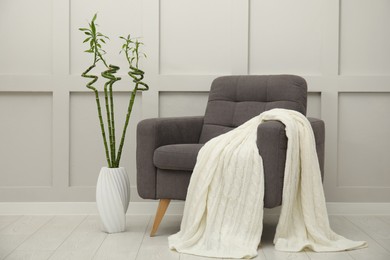 Photo of Vase with green bamboo stems on floor and armchair in room. Interior design