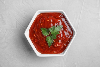 Photo of Bowl of hot chili sauce with parsley on light background, top view