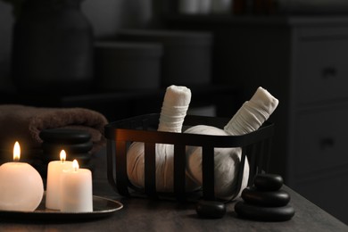 Photo of Herbal massage bags, burning candles and stones on grey table. Spa products