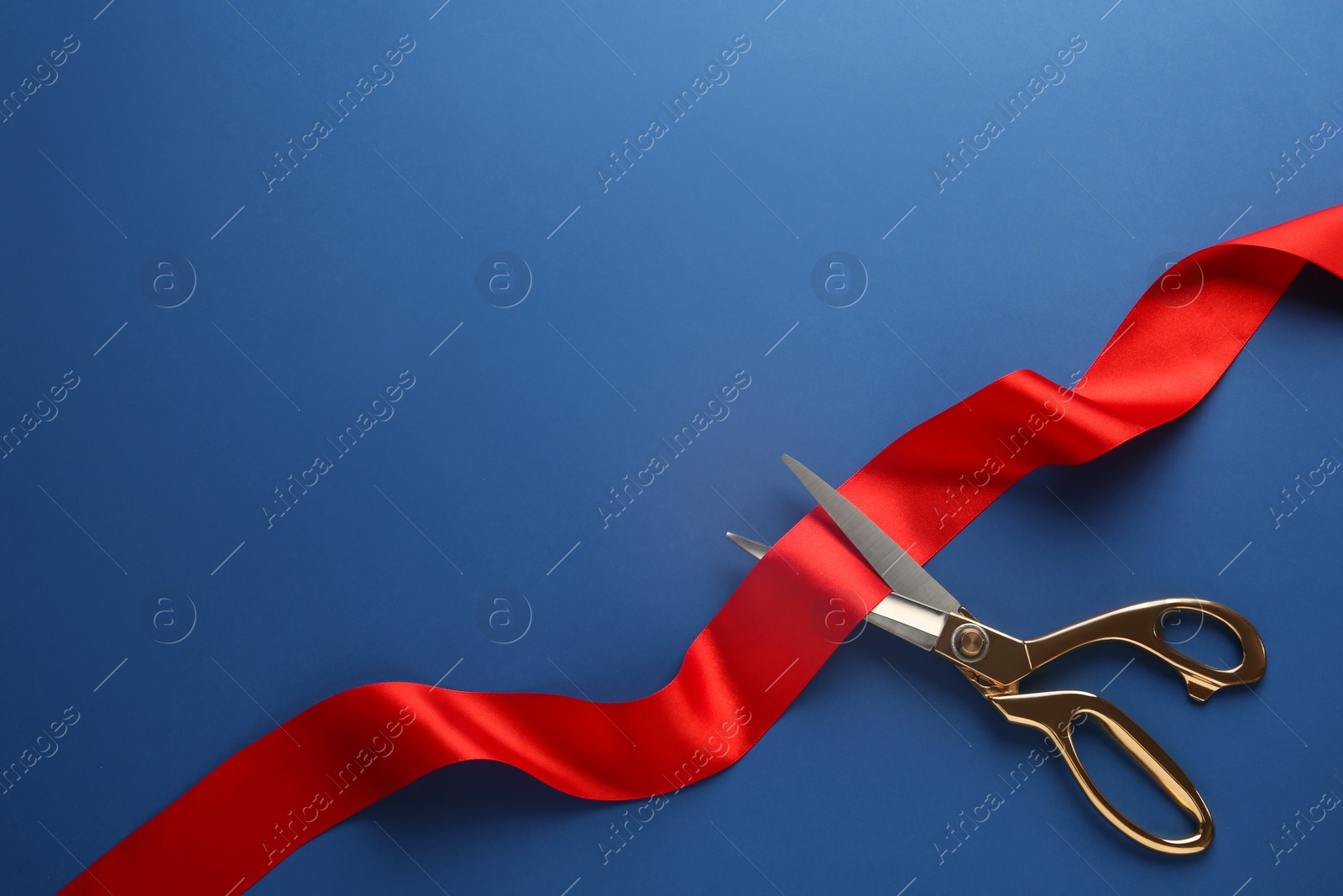 Photo of Red ribbon and scissors on blue background, top view. Space for text