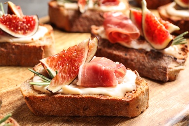 Photo of Bruschettas with cream cheese, prosciutto and figs served on wooden board, closeup