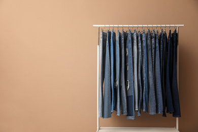 Photo of Rack with stylish jeans near beige wall. Space for text