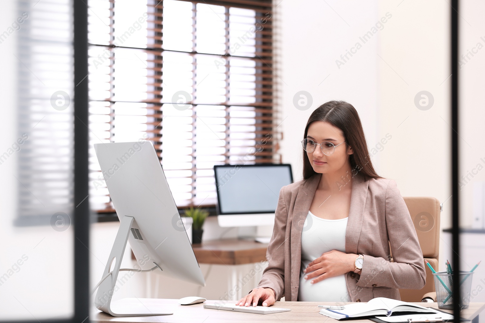 Photo of Young pregnant woman working with computer at table in office