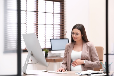 Photo of Young pregnant woman working with computer at table in office