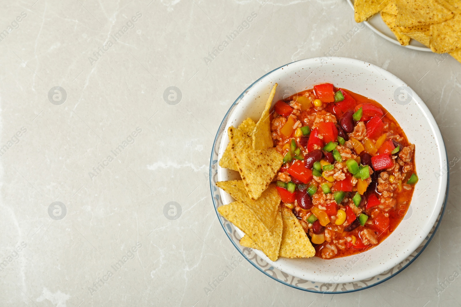 Photo of Chili con carne served with tortilla chips on grey table, top view. Space for text