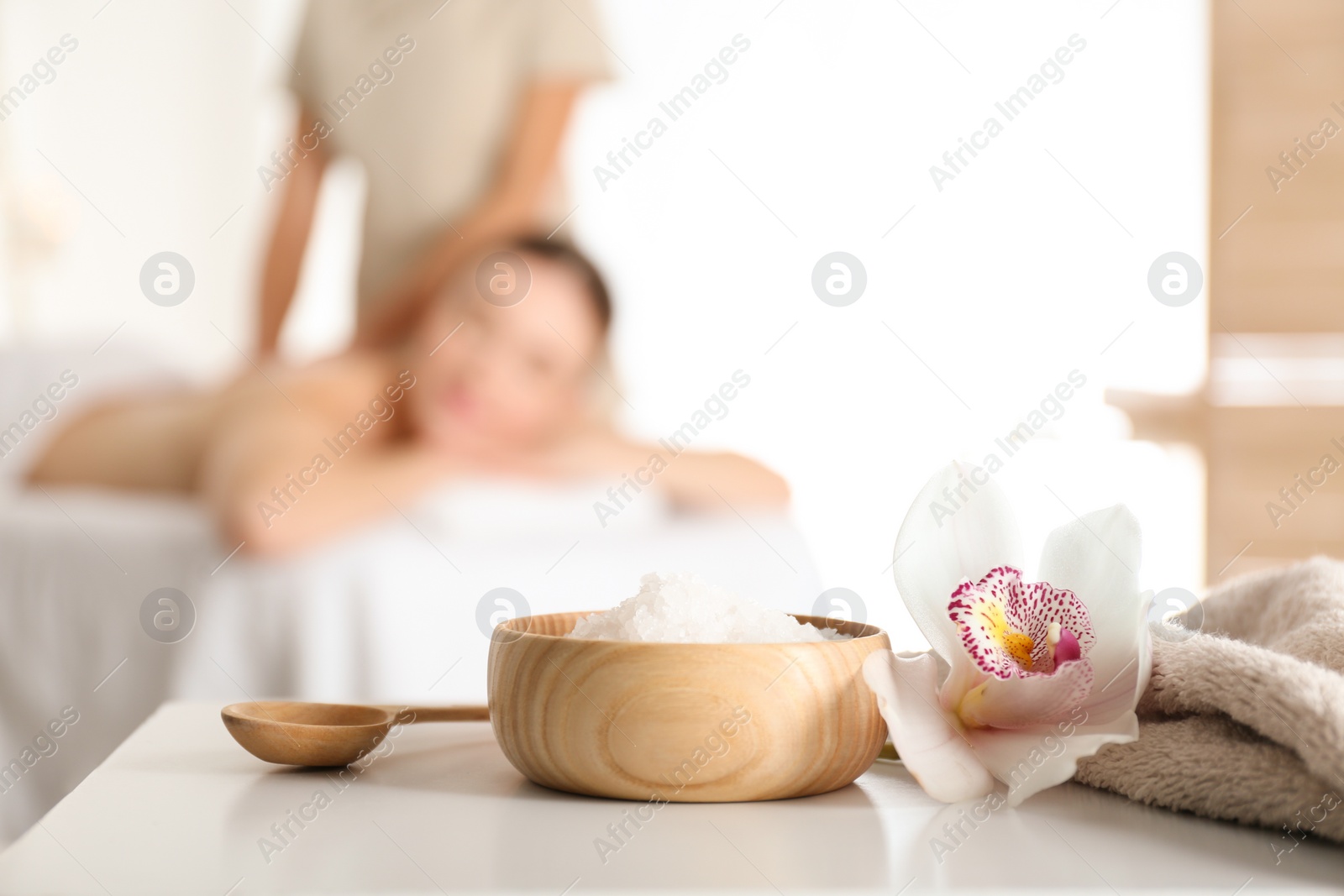 Photo of Bowl with sea salt and orchid flower on white table in spa salon. Space for text