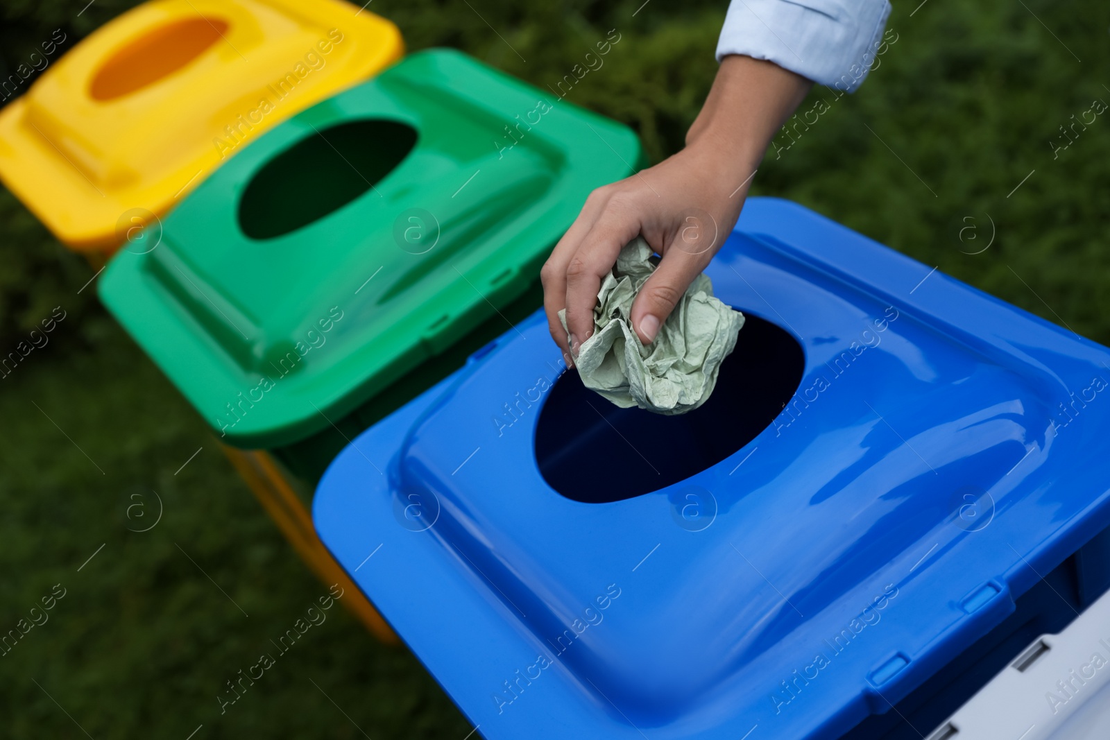 Photo of Woman throwing crumpled tissue into recycling bin outdoors, closeup