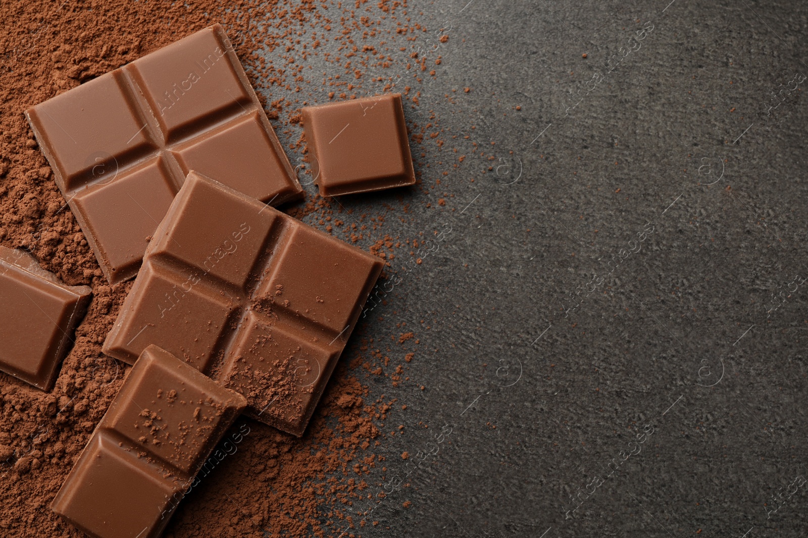 Photo of Delicious milk chocolate and cocoa powder on grey table, flat lay. Space for text