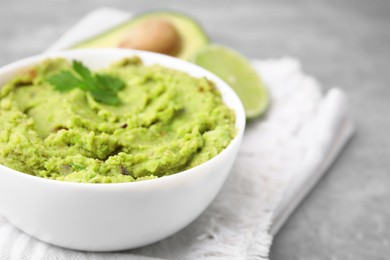 Photo of Bowl of delicious guacamole and ingredients on grey table, closeup. Space for text