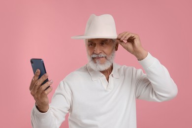 Photo of Senior man in hat using smartphone on pink background