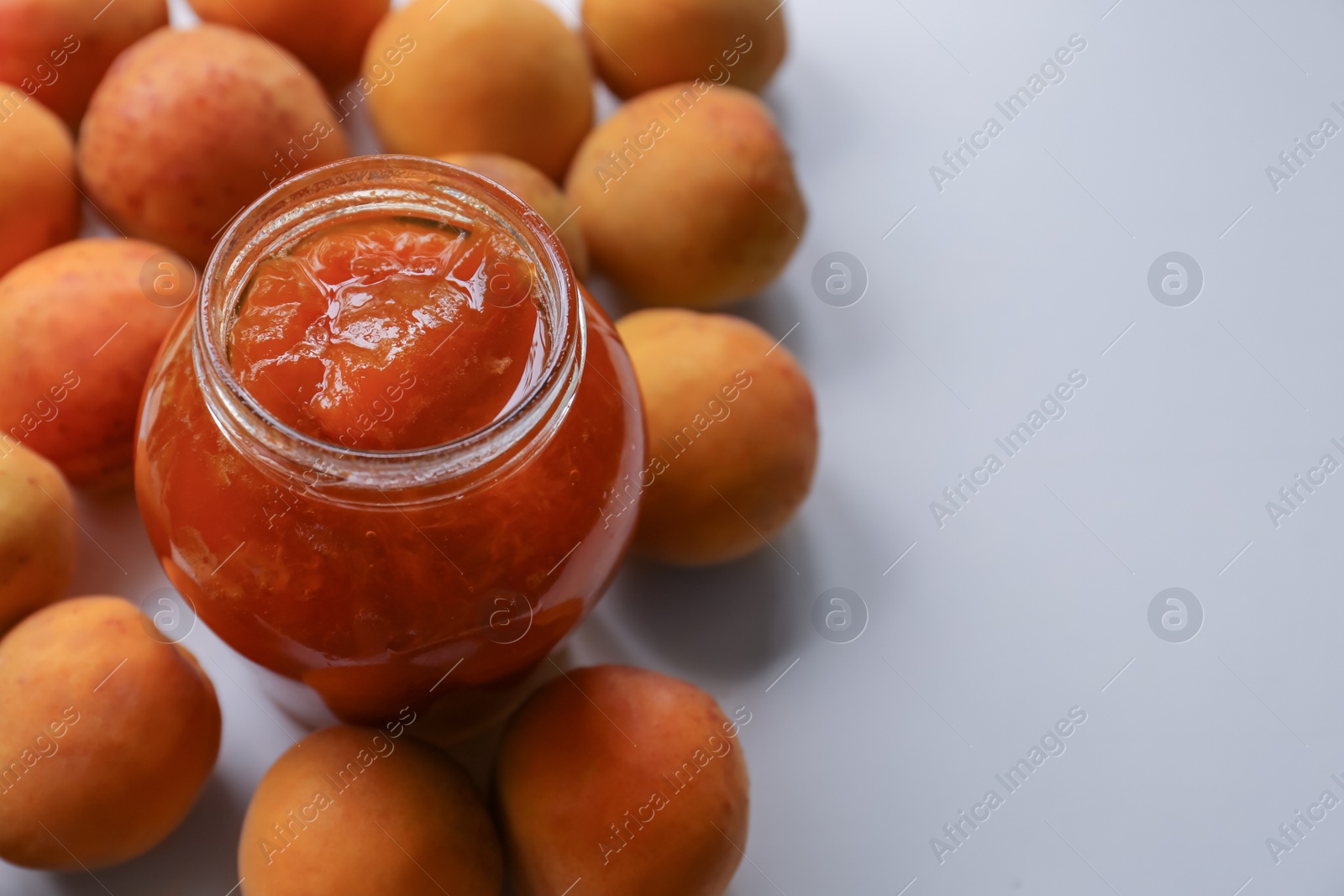 Photo of Jar of delicious jam and fresh ripe apricots on white background, space for text. Fruit preserve