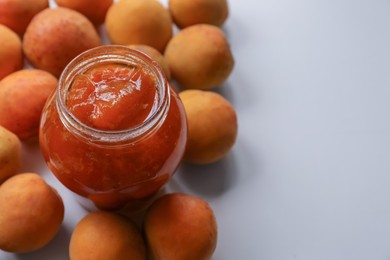 Photo of Jar of delicious jam and fresh ripe apricots on white background, space for text. Fruit preserve