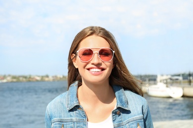 Photo of Young woman wearing stylish sunglasses near river